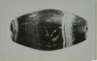 Oval banded bead with a dark glossy body and pale stripes, small find from Idalion