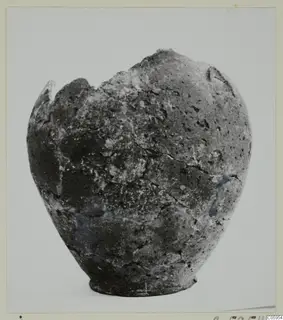 Hand-made coarse pottery vessel with a broken rim, photographed against a plain light background