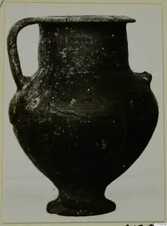 Pottery Black-on-Red vessel with a single handle, a flared rim and a footed base, shown against a pale background.