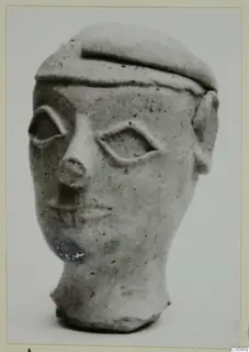 Terracotta head figurine from Ayia Irini with a flat cap-like top and almond-shaped eyes, shown against a plain background