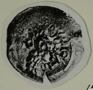 Round corroded object with raised circular and curled motifs, shown on a mounted card; find from Idalion.