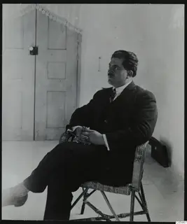 Mr. Kaplanis, mayor of Lapithos, seated in a wicker chair in front of a panelled door