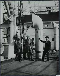 Two men on the deck of M/S Gotland at Famagusta, beside a large white ventilator pipe and coiled ropes.