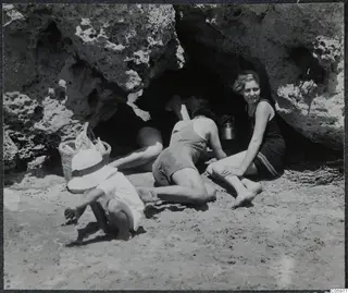 Four people at the mouth of a small rock cave on a sandy beach in Kyrenia, one crouching in the foreground.