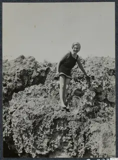 Gudrun Atterman in a dark swimsuit on rough rocks in Kyrenia, smiling at the camera