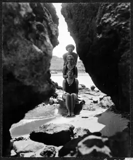 Three women posing one above another between rock walls on a rocky beach in Kyrenia