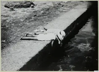 Two children lie stretched along a stone edge, playing with the water of a rock pool below them.