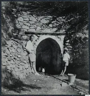 Man and boy standing beside a stone-arched water source at Machairas