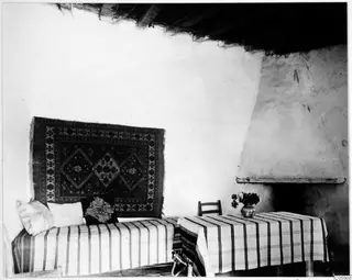 Interior of a house at Machairas with a striped-covered sofa, a hanging rug and a white fireplace on the right