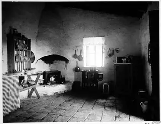 Interior of a house kitchen at Machairas with a hearth niche, a small stove and hanging pans