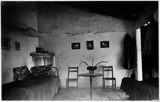 Interior of a whitewashed room at Machairas with two beds, a round table and two wooden chairs