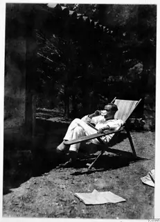 A man in white clothes drinks from a cup while seated in a wooden deck chair on the terrace at Machairas.
