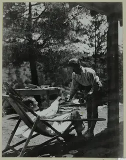 Two men on a terrace at Machairas: one reclines in a deck chair while the other offers him a slice of cake.