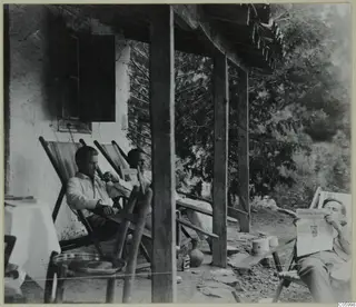 Three men resting in deck chairs on a stone-floored porch of the expedition house at Machairas.