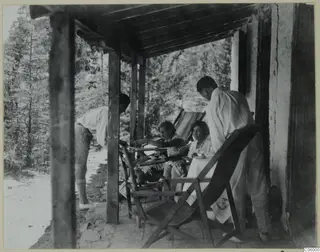 Four people eating on a timber-posted terrace outside a whitewashed house at Machairas, with pine trees behind.