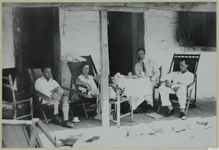 Four people relax on deck chairs and at a table on a stone-walled veranda at Machairas.