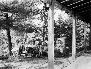 Four people resting in deck chairs on a terrace at Machairas, with tall pine trees behind them.