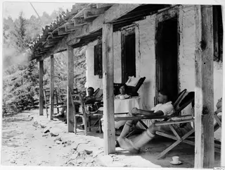 People resting on deckchairs on the terrace of a whitewashed house at Machairas, with a woman seated at a table
