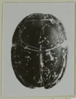 Dark stone scarab seal seen from above, with a horizontal line across its head and a central groove along its back.