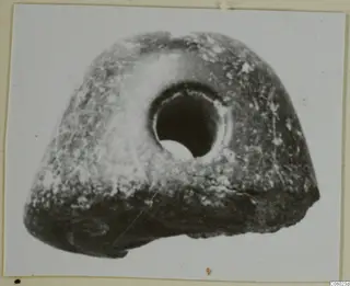 Pierced stone object with a large round hole through its upper centre, shown on a mounted print