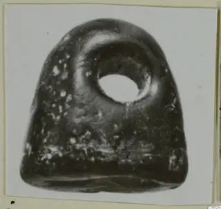 Dark polished stone object with a large perforation near its top, a glyptic find