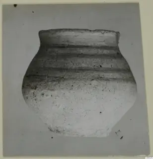 Pottery jar with a short flaring neck and dark horizontal bands, photographed against a plain grey background