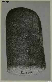 Pestle, a dark stone object with a rounded top, photographed upright against a grey backdrop