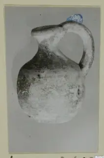 Small jug with a strap handle and a wide spout, photographed against a grey background on a card mount