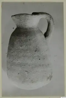 Plain white pottery jug with a strap handle, shown against a grey backdrop