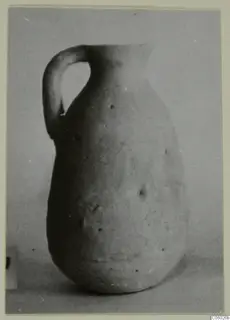 Plain pale pottery jug with a strap handle and narrow neck, photographed against a grey backdrop.