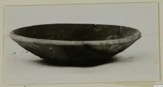 Shallow coarse pottery bowl with a pale rim band and a broken section on the rim.