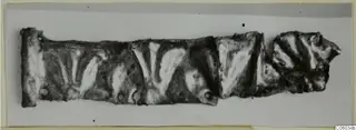 Fragmentary silver strip with raised chevron pattern, made of several joined pieces, lying flat on a pale ground