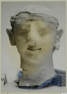 Frontal view of a pale head and bust of a figure with a flat headdress and round earrings