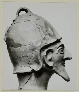 Terracotta head of a statue from Ayia Irini, shown in profile, wearing a helmet-like cap with a loop on top.