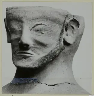 Terracotta Proto-Cypriote I statuette: head with a flat-topped headdress, beard along the jaw and large ear, seen in three-quarter view.