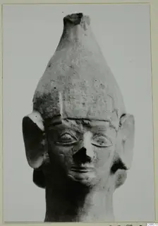 Terracotta head of a figurine with a tall conical headdress, large flat ears and a broken nose
