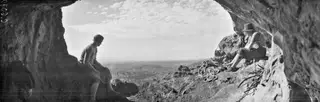 Two men seated at the mouth of a cave at Fylleri, Kythrea, with coiled ropes beside them and hills in the distance.