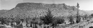 Flat-topped rock ridge at Fylleri above water and tall trees, near Kythrea