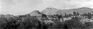 Panoramic view of the village of Fylleri, with flat-roofed houses among trees and bare hills behind it