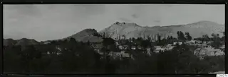 Panoramic view of the village of Fylleri, houses among trees below bare pale hills.