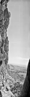 Steep rock face at Fylleri with a climber on the cliff, and a hazy valley with trees and hills below