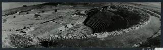 Panoramic view of the theatre at Soli, with curved tiered seating cut into a hillside and stone walls around it.