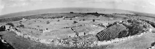 Panoramic view over the theatre at Soli, with curving stone seating and walls in the foreground, fields and the sea beyond