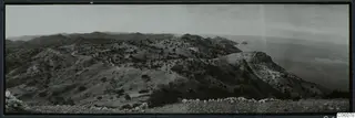 Panoramic view over hilly land with a winding track and the sea on the right, seen from Vouni.