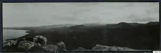 Panoramic view from rocky heights over a coastal bay and dark hills towards Soli, with boulders in the foreground.
