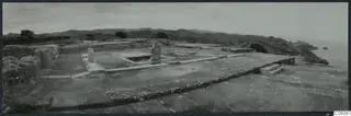 Central court at Vouni from the east: paved floor, a standing stone object, low walls, steps, with hills and sea beyond.