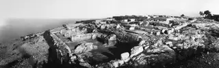 Panoramic view of the palace at Vouni from the west, with walls and stone blocks across a hilltop above the sea.