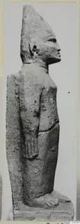 Limestone Cypro-Egyptian statue of a standing figure in side profile, wearing a tall pointed headdress.