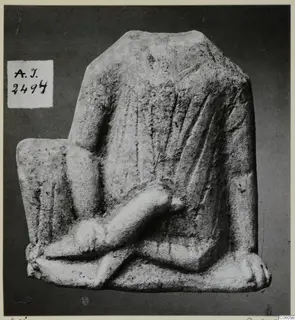 Limestone figurine fragment with a draped body and a crossed arm or leg, against a dark background