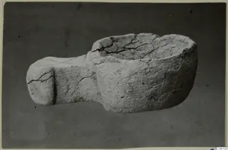 Stone bowl with a flat projection on one side, cracked, photographed against a dark backdrop